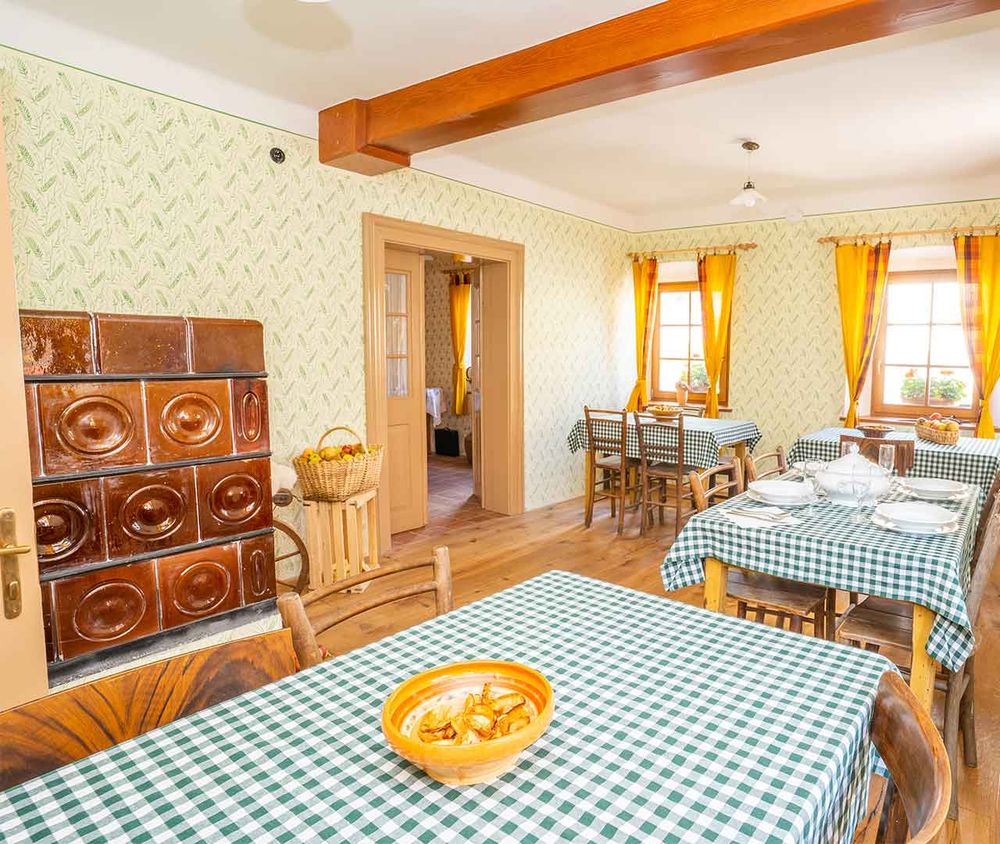 Tradicionalna jedilnica v Notranjski hiši s krušno pečjo, lesenimi tramovi in pogrnjenimi mizami.
